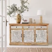 elegancka aranżacja jasnego salonu w stylu komoda boho z rzeźbioną biało naturalną komodą indyjską ozdobioną wazonem z gałązkami i lampą stojącą