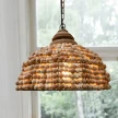 lampa drewniana z koralikow powieszona w jasnym salonie na tle okna