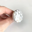 Detal uchwytu ceramicznego biało-złotego na tle drewnianej szuflady