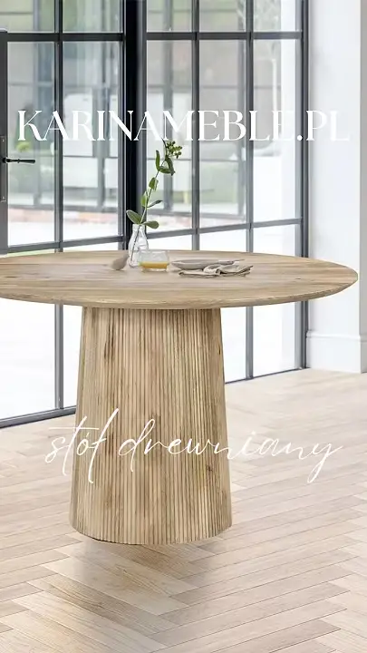 Prezentacja wideo: Okrągły stół z jasnego drewna mango z grubą, ryflowaną podstawą w kształcie walca, ozdobiony wazonem z gałązką i naczyniami, zaprezentowany w zalanym słońcem, przestronnym wnętrzu z drewnianą podłogą w jodełkę na tle dużych, czarnych okien – Styl Japandi